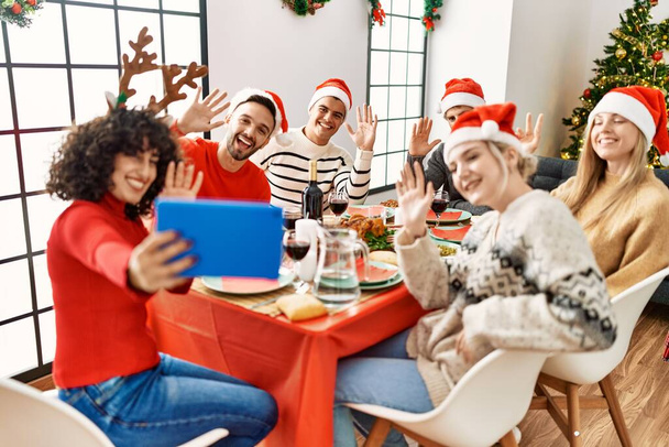 Joukko nuoria, jotka viettävät jouluaterian ja videopuhelun kotona kosketuslevyn avulla. - Valokuva, kuva