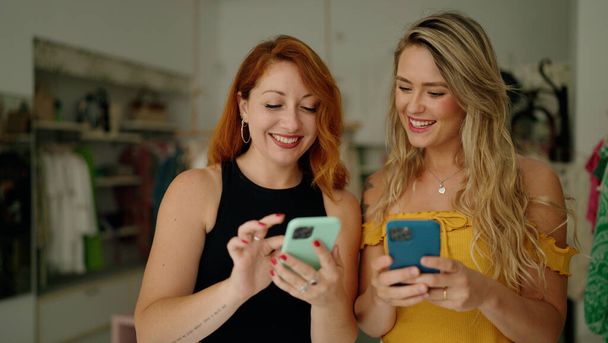 Zwei Frauen lächeln im Bekleidungsgeschäft selbstbewusst mit Smartphones - Foto, Bild