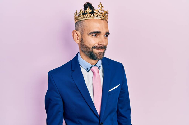 Jovem hispânico vestindo roupas de negócios e coroa rei olhando para o lado, relaxar pose perfil com rosto natural e sorriso confiante.  - Foto, Imagem