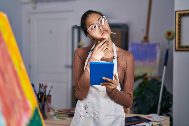 若いアフリカ系アメリカ人女性アーティストがアートスタジオで疑わしい表現でタッチパッドを使う - 写真・画像