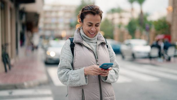 Mujer hispana de mediana edad sonriendo confiada usando smartphone en la calle - Foto, Imagen