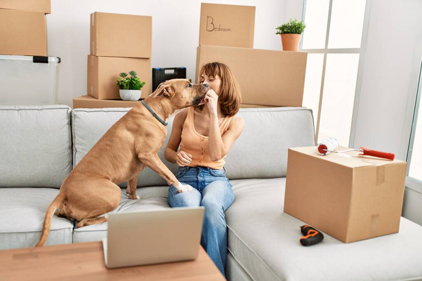 Молодая белая женщина с ноутбуком сидит дома на диване с собакой - Фото, изображение