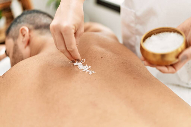 Young hispanic man having back massage using salt at beauty center - Fotó, kép