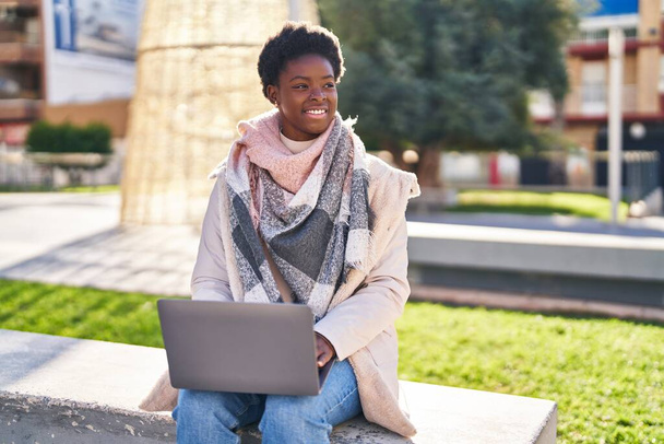 African american woman using laptop sitting on bench at park - Foto, immagini