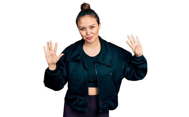 Young hispanic girl wearing sportswear showing and pointing up with fingers number nine while smiling confident and happy.  - Foto, imagen