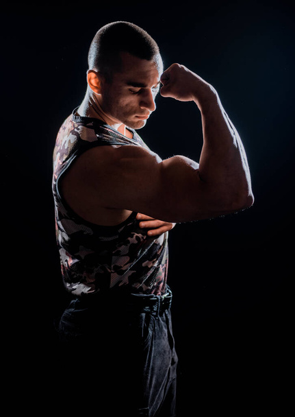 Portrait of young muscular man is flexing his muscles on dark background - Fotó, kép