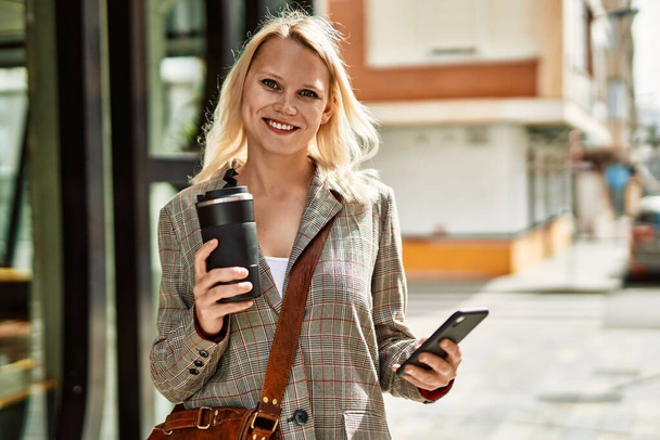 Молода блондинка, використовуючи смартфон, п'є каву в місті
. - Фото, зображення