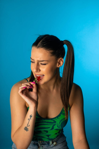 Pretty girl bites the cherry gummy in the studio - Φωτογραφία, εικόνα