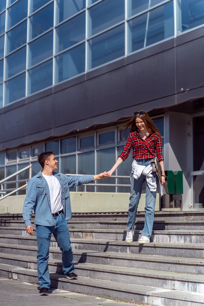 Hübsches Paar läuft auf der Treppe vor dem Gebäude und hält Händchen und lächelt - Foto, Bild