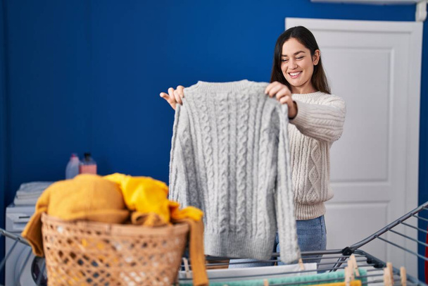 jonge vrouw glimlachen zelfverzekerd opknoping kleren op waslijn in wasruimte - Foto, afbeelding