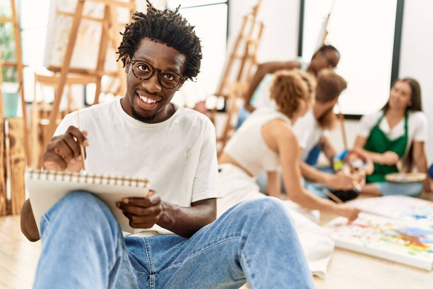 Grupo de personas sonriendo feliz dibujo sentado en el suelo en el estudio de arte. - Foto, Imagen