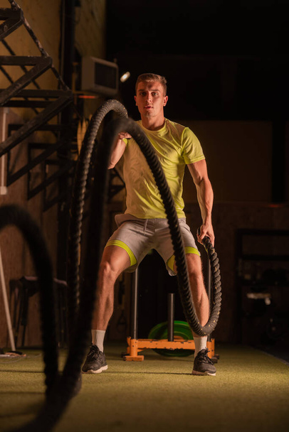 Schöner und fitter Kerl trainiert auf den Seilen in der Turnhalle - Foto, Bild