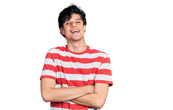 Handsome hipster young man wearing casual striped t shirt happy face smiling with crossed arms looking at the camera. positive person.  - 写真・画像