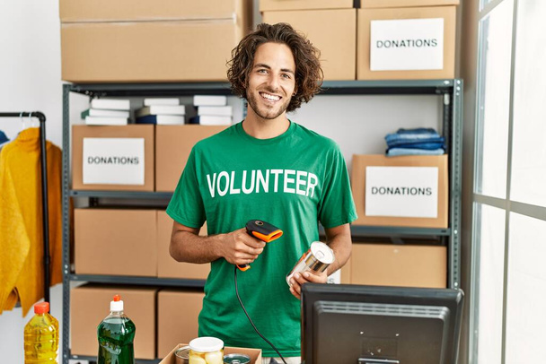 Joven voluntario hispano sonriendo feliz trabajando en el centro de caridad. - Foto, imagen