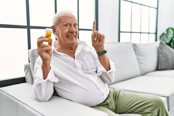 Senior man met pillen die de vinger wijzen met een succesvol idee. opgewonden en gelukkig. Nummer een.  - Foto, afbeelding