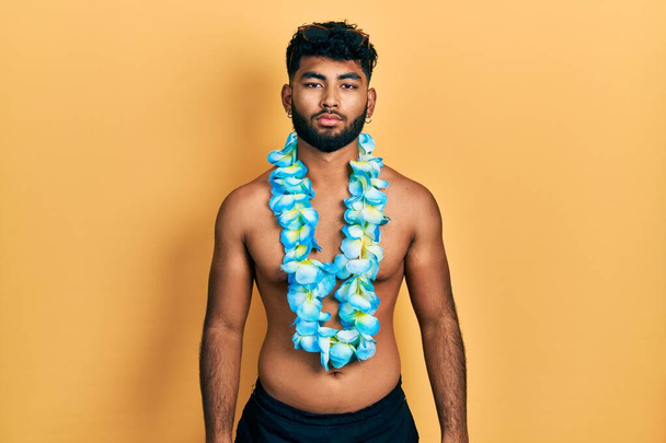 Arab man with beard wearing swimsuit and hawaiian lei with serious expression on face. simple and natural looking at the camera.  - Foto, Imagem