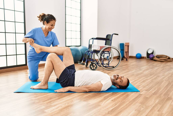 Muž středního věku a žena se usmívá sebevědomě s rehabilitační sezení protahování na fyzioterapii - Fotografie, Obrázek