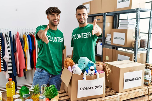 Ein junges schwules Paar im freiwilligen T-Shirt am Spendenstand lächelt freundlich und reicht zur Begrüßung Handschlag. Erfolgreiches Geschäft.  - Foto, Bild