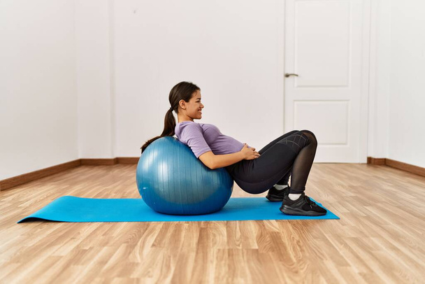 Young latin woman doing abs exercise using fit ball at sport center - Photo, Image