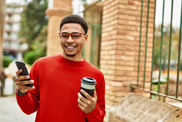 Knappe Afrikaanse Amerikaanse man buiten met behulp van smartphone typen van een bericht - Foto, afbeelding