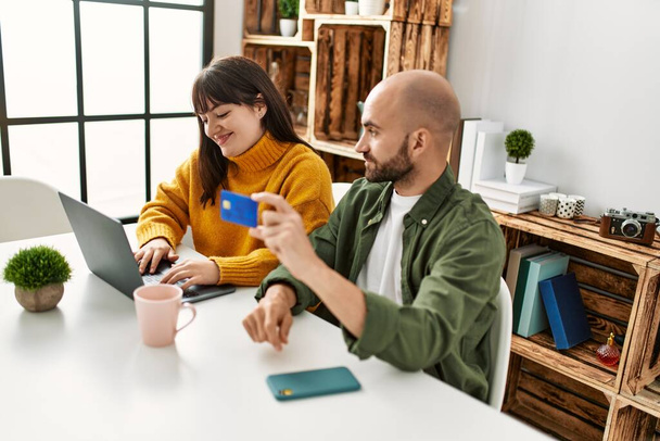 Giovane coppia ispanica sorridente felice con computer portatile e carta di credito seduto sul tavolo a casa. - Foto, immagini