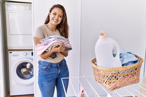 Молода іспаномовна дівчина займається пранням, тримаючи складений одяг вдома
. - Фото, зображення