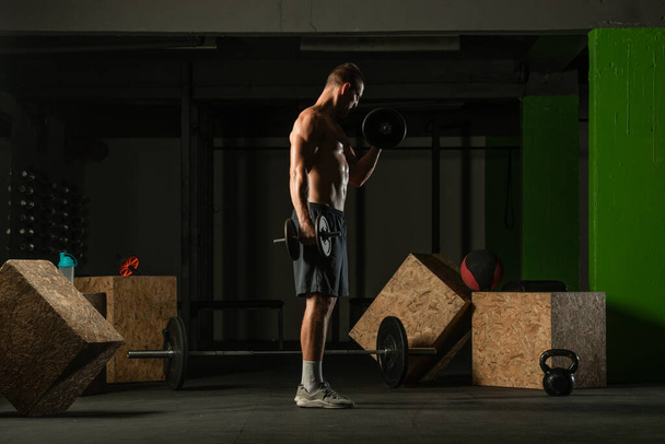 Foto vista lateral de um jovem fisiculturista formação dumbbell alternar bíceps curl em casa ginásio - Foto, Imagem