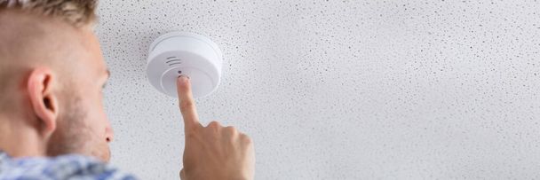 Low Angle View Of A Person's Hand Installing Smoke Detector On Ceiling Wall At Home - Foto, afbeelding