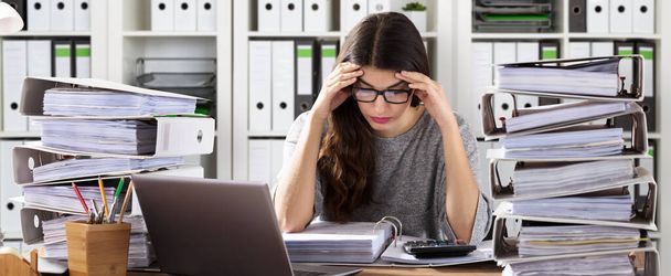 Worried Businesswoman Working At Office With Stack Of Folders On Desk - 写真・画像