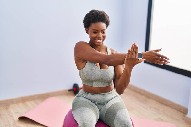African american woman smiling confident stretching arm at sport center - Photo, Image