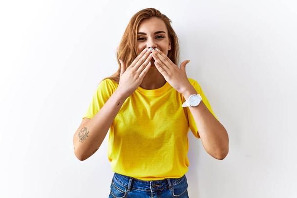 Young brunette woman standing over isolated background laughing and embarrassed giggle covering mouth with hands, gossip and scandal concept  - Foto, afbeelding