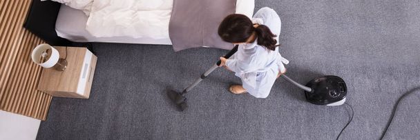 Happy Young Housekeeper Cleaning Carpet With Vacuum Cleaner In Hotel Room - Φωτογραφία, εικόνα