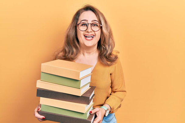 Žena středního věku běloška drží hromadu knih s úsměvem a hlasitě se směje, protože vtipný bláznivý vtip.  - Fotografie, Obrázek
