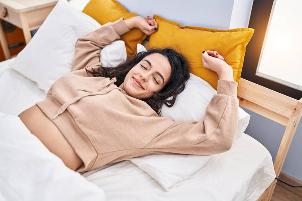 Jeune femme hispanique étirant les bras allongés sur le lit dans la chambre - Photo, image
