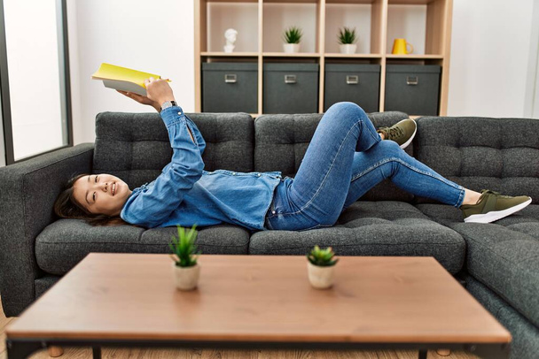 Молодая китаянка читает книгу, лежащую дома на диване.. - Фото, изображение