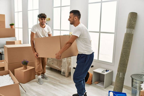 Two hispanic men couple smiling confident holding cardboard box at new home - Photo, Image