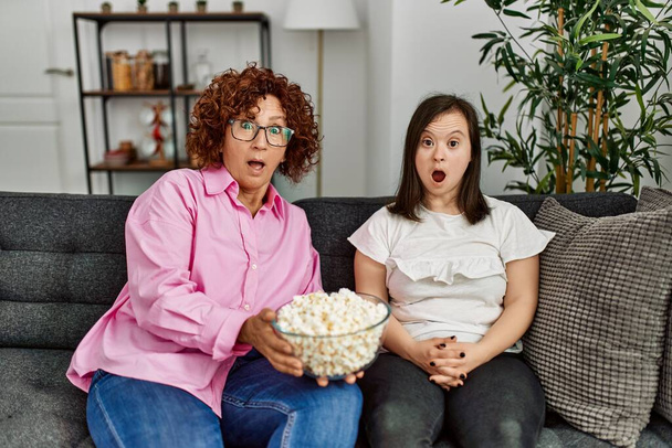 Madura madre y abajo síndrome hija en casa comer palomitas de maíz y ver la televisión - Foto, imagen