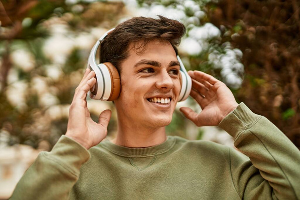 Młody Latynos uśmiecha się szczęśliwy używając słuchawek w mieście. - Zdjęcie, obraz