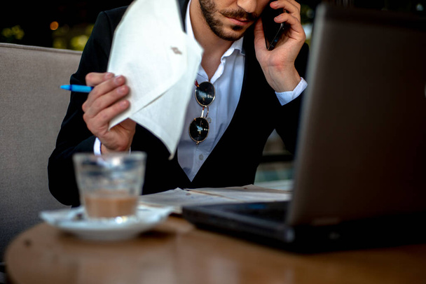 Detalles de un hombre de negocios trabajando y hablando por teléfono mientras se sienta en la cafetería - Foto, imagen