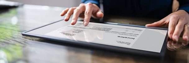 Close-up Of A Businessperson's Hand Analyzing Bill On Digital Tablet Over Desk - Foto, afbeelding