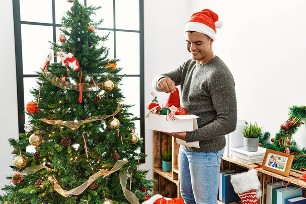 Fiatal spanyol férfi mosolygós magabiztos díszítő karácsonyfa otthon - Fotó, kép
