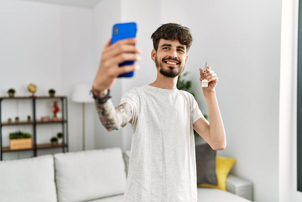 Młody Latynos robi selfie przy smartfonie z kluczem do nowego domu - Zdjęcie, obraz