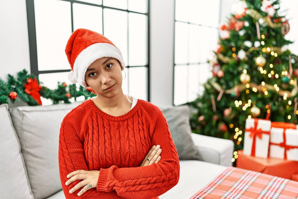 Young hispanic woman with short hair wearing christmas hat sitting on the sofa looking sleepy and tired, exhausted for fatigue and hangover, lazy eyes in the morning.  - Fotografie, Obrázek