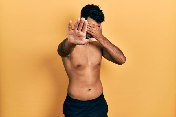 Arab man with beard wearing swimwear shirtless covering eyes with hands and doing stop gesture with sad and fear expression. embarrassed and negative concept.  - Foto, immagini