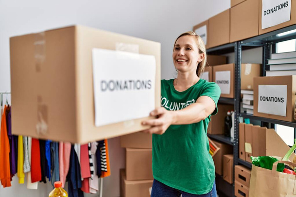 Young caucasian woman wearing volunteer uniform holding donations package working at charity center - Photo, image