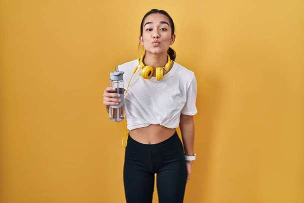 Young south asian woman wearing sportswear drinking water looking at the camera blowing a kiss on air being lovely and sexy. love expression.  - 写真・画像
