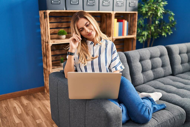 Giovane donna bionda che utilizza il computer portatile seduto sul divano a casa - Foto, immagini