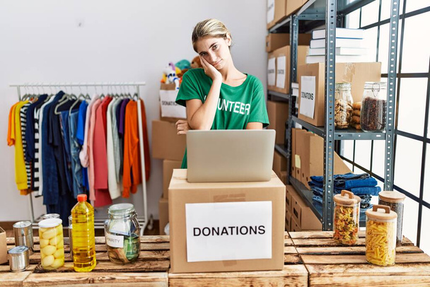 Young blonde woman wearing volunteer t shirt at donations stand thinking looking tired and bored with depression problems with crossed arms.  - Photo, Image
