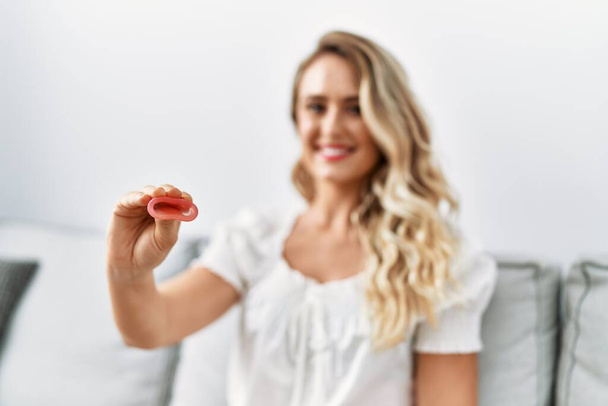 Young woman holding menstrual cup sitting on sofa at home - Photo, Image