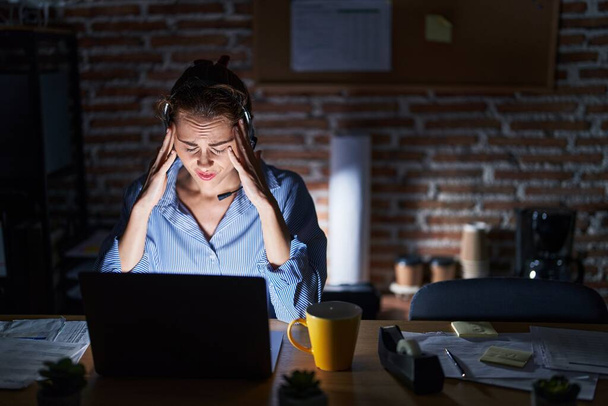 Beautiful brunette woman working at the office at night with hand on head for pain in head because stress. suffering migraine.  - Photo, Image